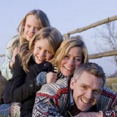 En familie, der ligger oven på hinanden. De smiler til kameraet og er glade.