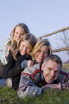 En familie, der ligger oven på hinanden. De smiler til kameraet og er glade.