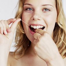 Kvinde, der bruger tandtråd. Hun smiler.