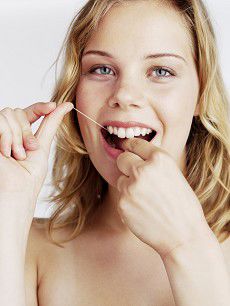 Kvinde, der bruger tandtråd. Hun smiler.