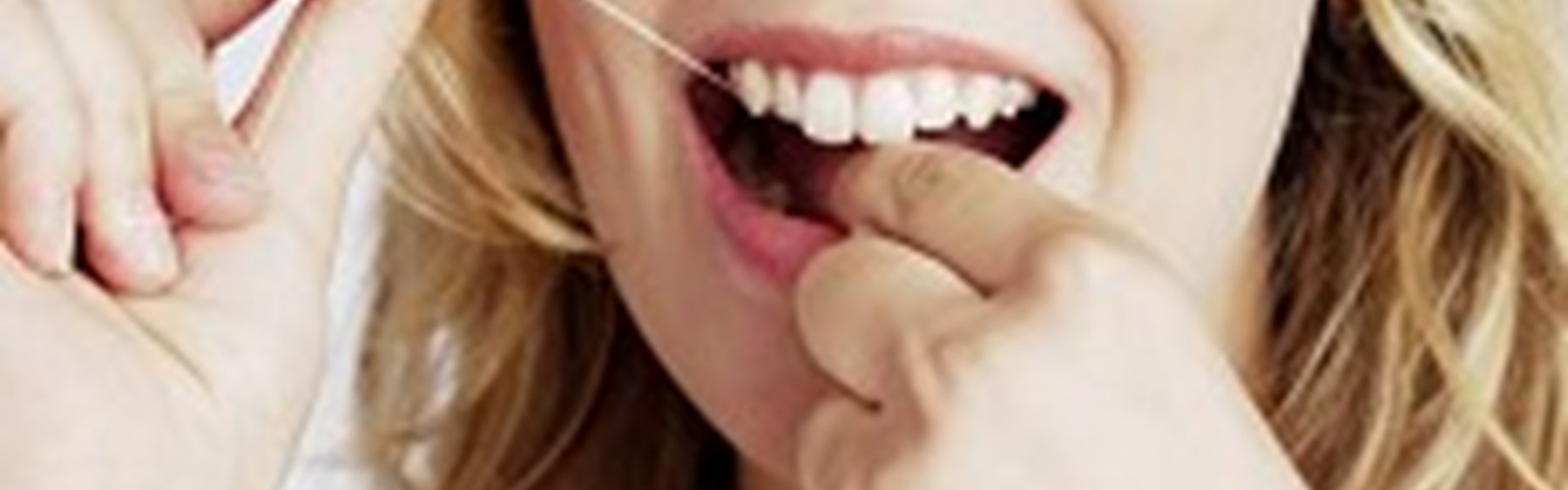 Kvinde, der bruger tandtråd. Hun smiler.