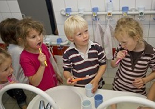 Fem børn, der børster tænder ved en håndvask.